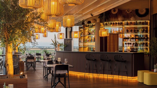 Um restaurante com piso de madeira, luminárias de vime pendentes e um bar com prateleiras cheias de garrafas.