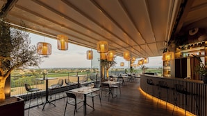 Uma área de refeições ao ar livre com mesas, cadeiras, um bar e vista para o campo.