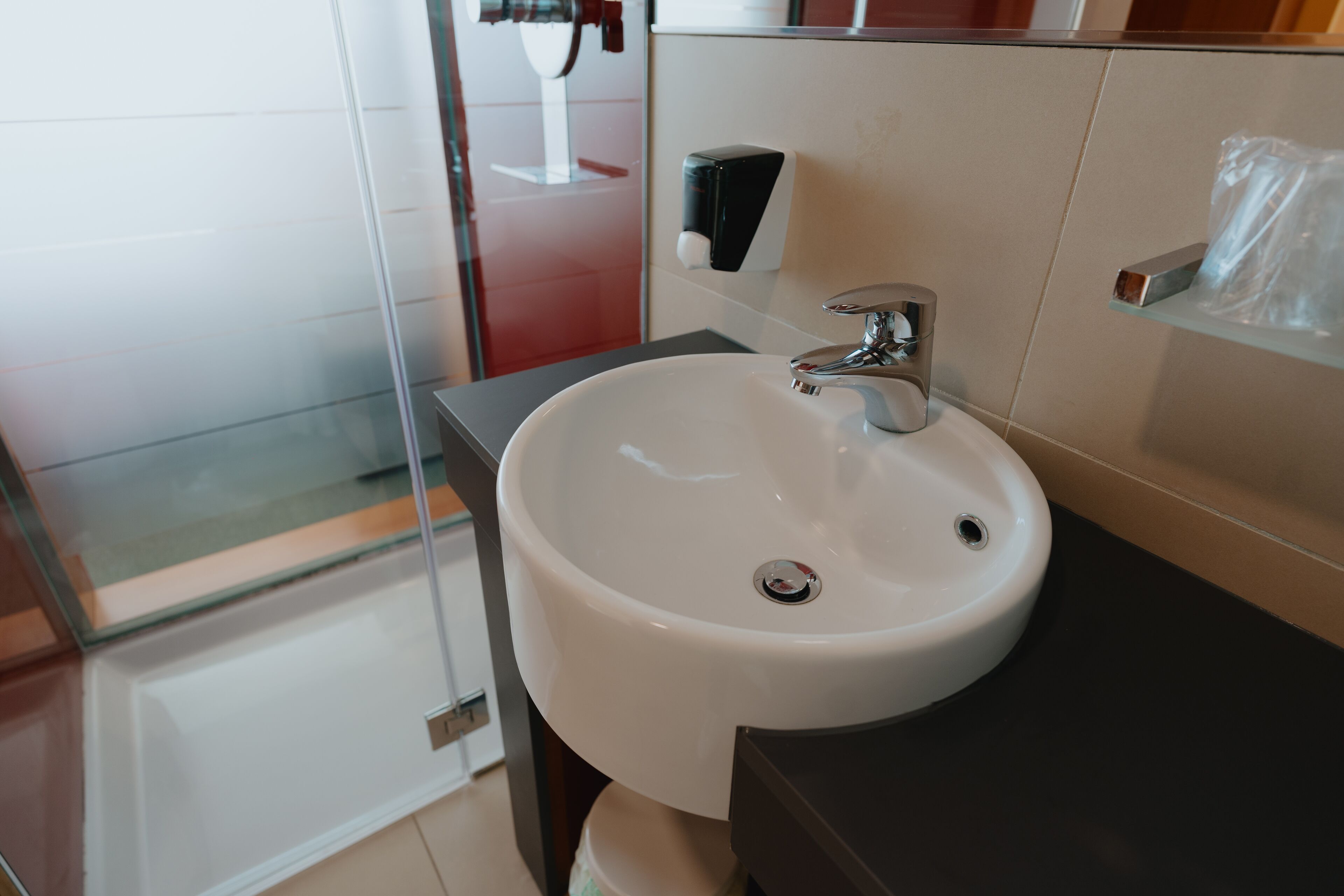 A bathroom with a white sink, a mirror, and a soap dispenser.