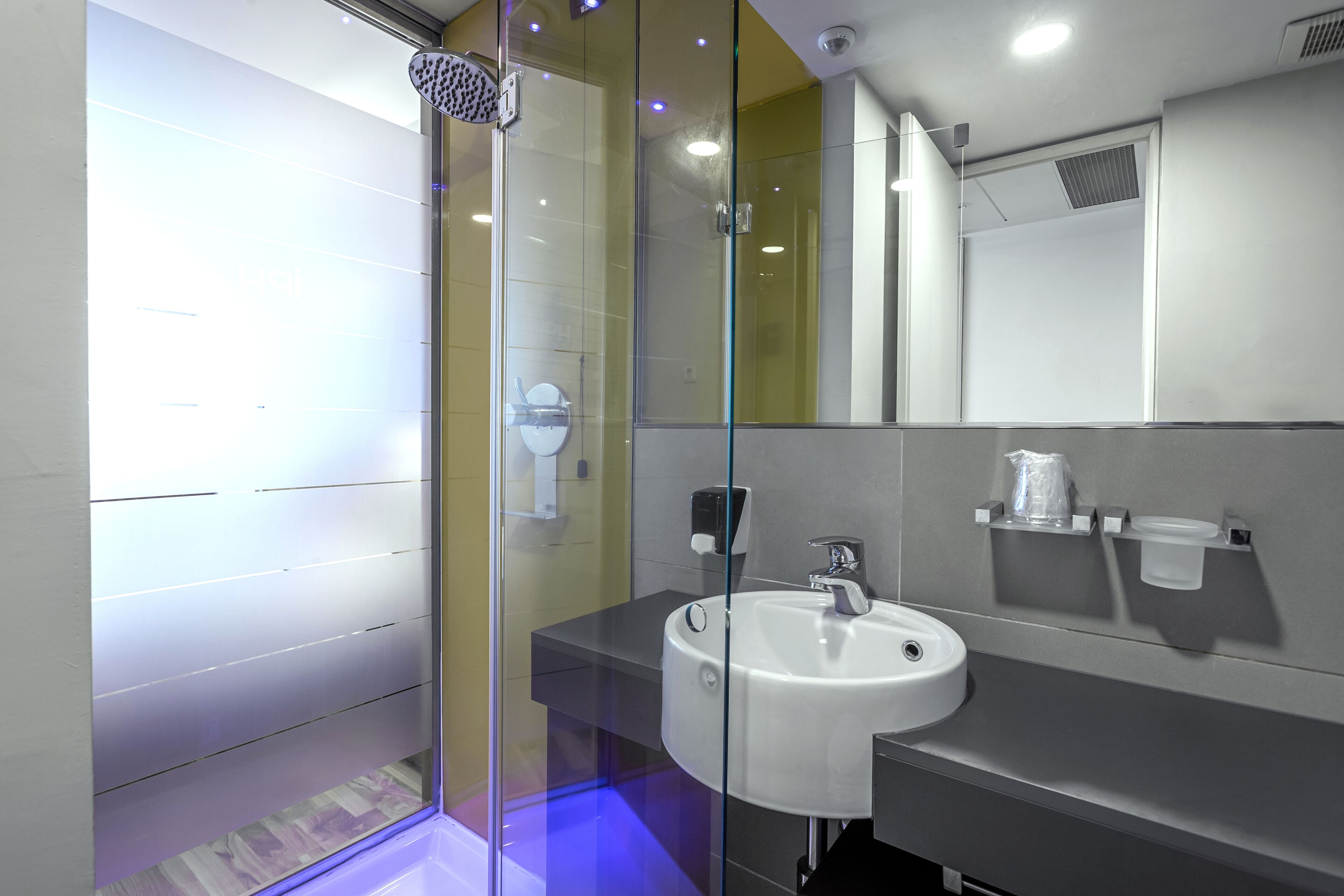 Un bany modern amb dutxa tancada amb vidre, un lavabo blanc i un mirall sobre el lavabo.