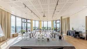 Uma sala de conferências com uma mesa grande, várias cadeiras e janelas amplas com vista para a cidade.