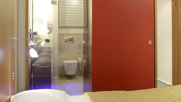 A hotel room with a bed, a red door, and a bathroom visible through a glass door.