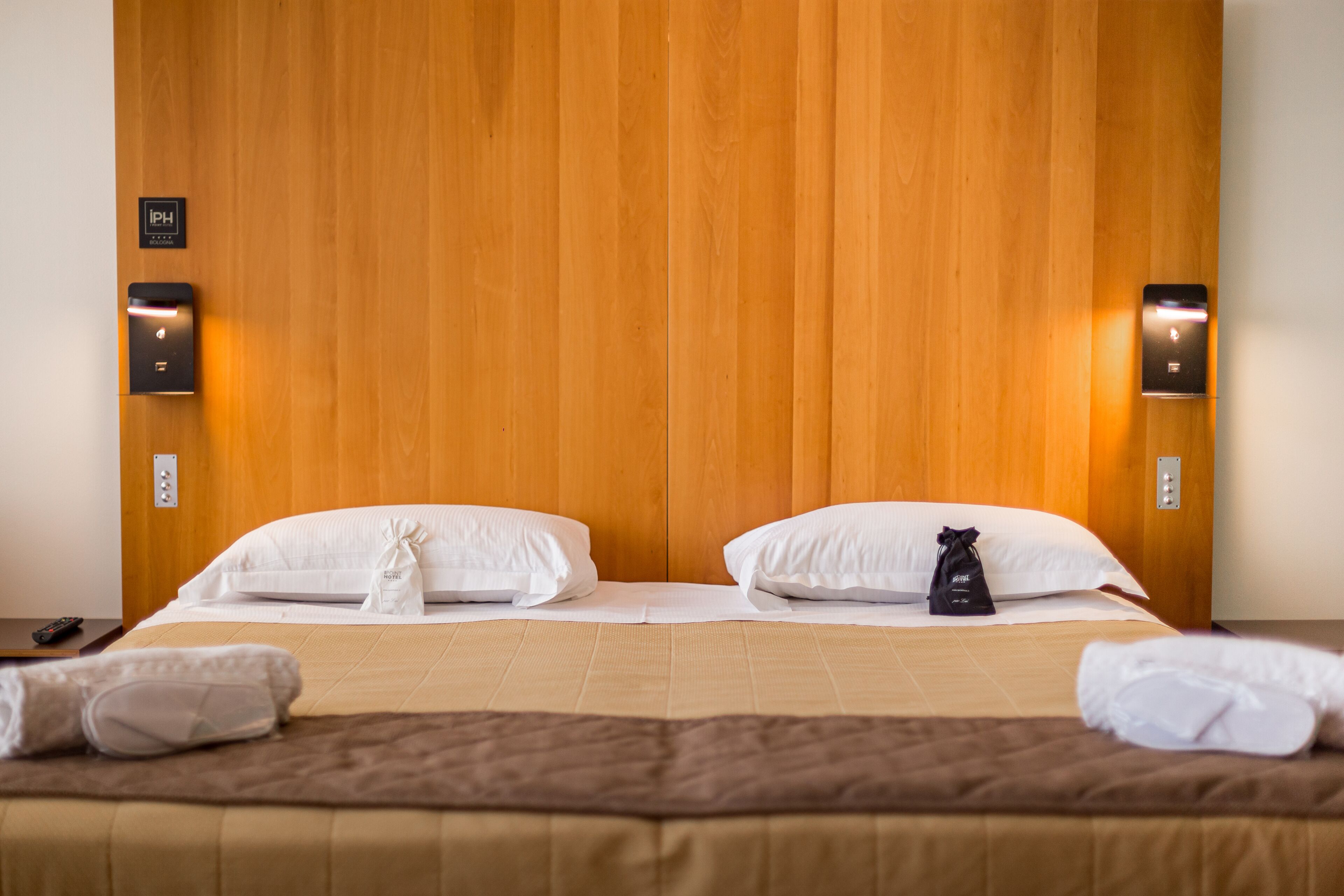 A hotel room with a wooden headboard, two white pillows, a brown bedspread, and a black bag on the bed.