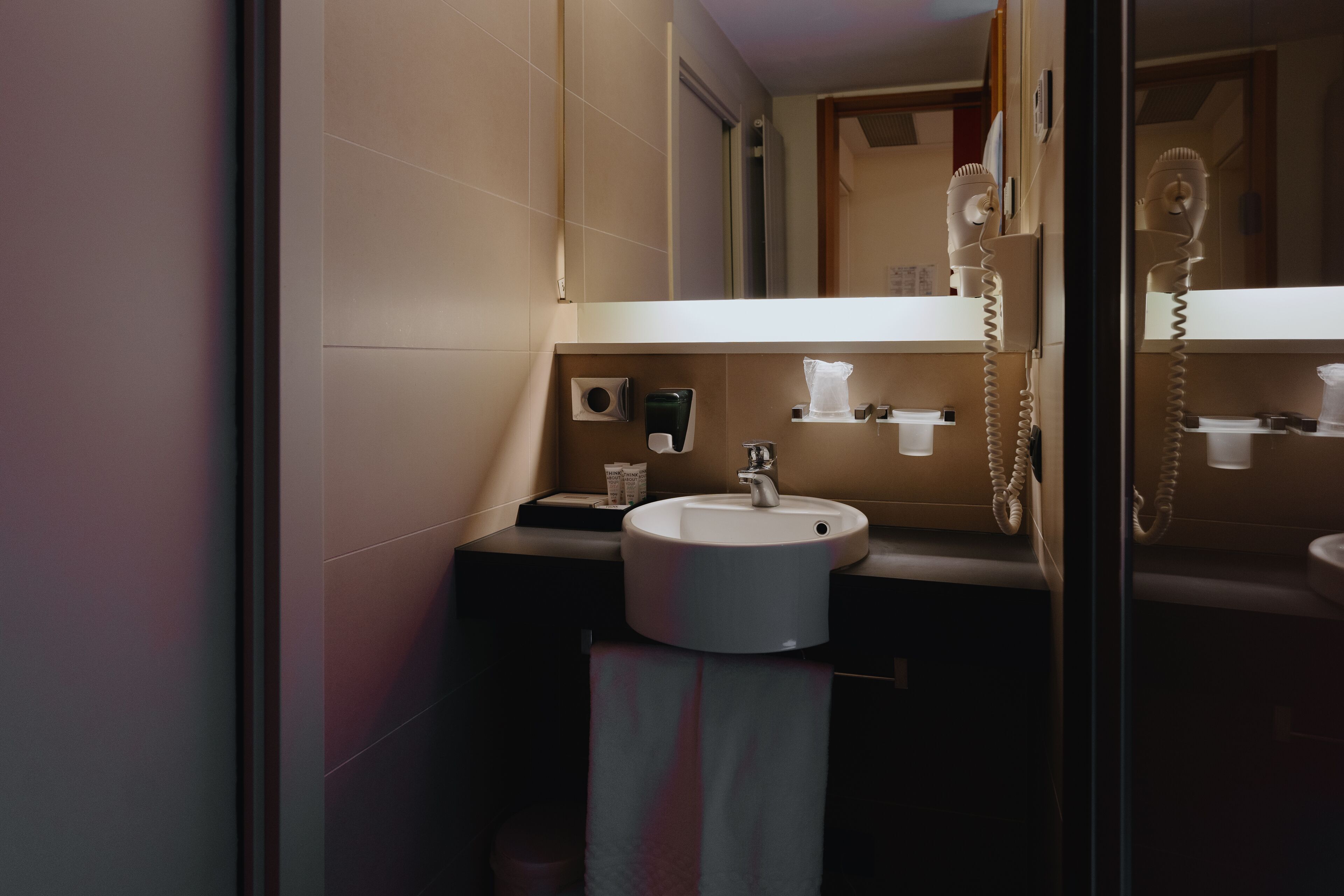 A modern bathroom with a round sink, a mirror, and a hairdryer mounted on the wall.