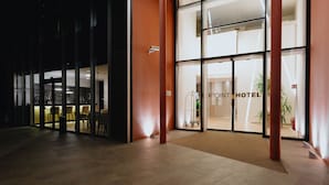 Entrada de um hotel com fachada de vidro, balcão de recepção e espaço interior com assentos.