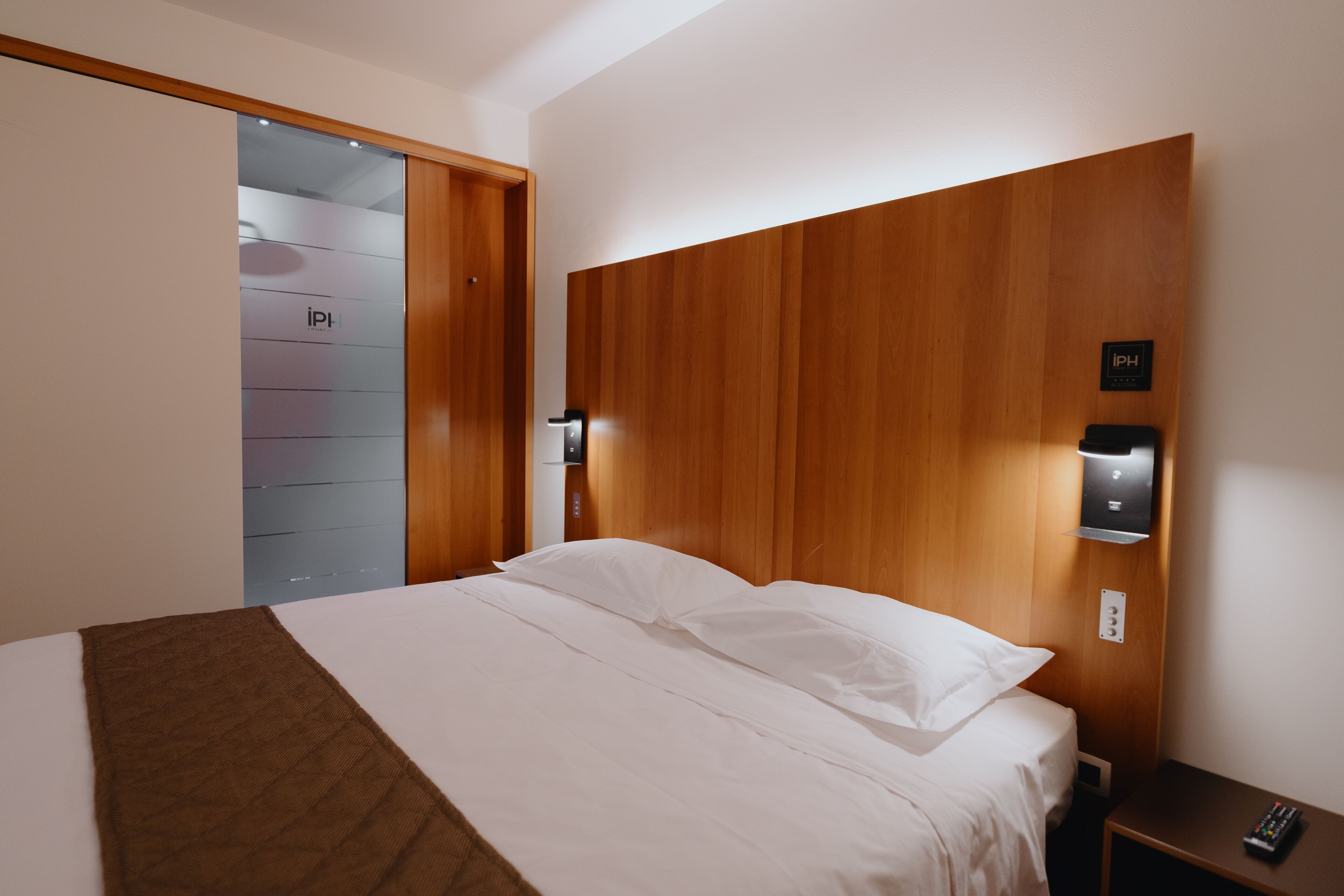 Habitació d'hotel moderna amb un llit gran, un panell de capçal de fusta i una taula de nit amb un comandament a distància.