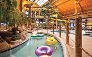 Un parc aquatique intérieur comprenant une piscine, des bouées gonflables et un espace de jeux en bois.