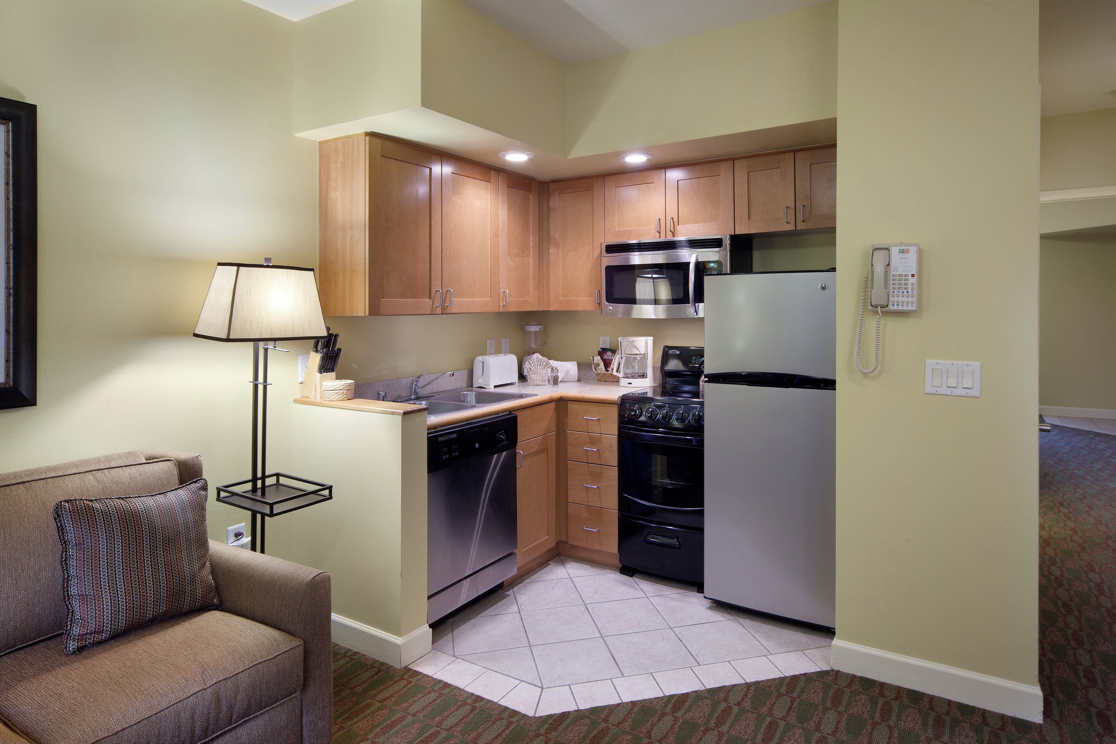 A compact kitchen with wooden cabinets, a microwave, a refrigerator, and a dishwasher.