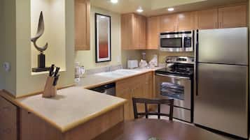 A modern kitchen with wooden cabinets, stainless steel appliances, a knife block, and a dining area with a chair.