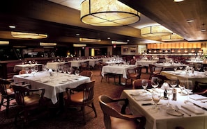 A restaurant with multiple tables set for dining, featuring overhead lighting and a patterned carpet.