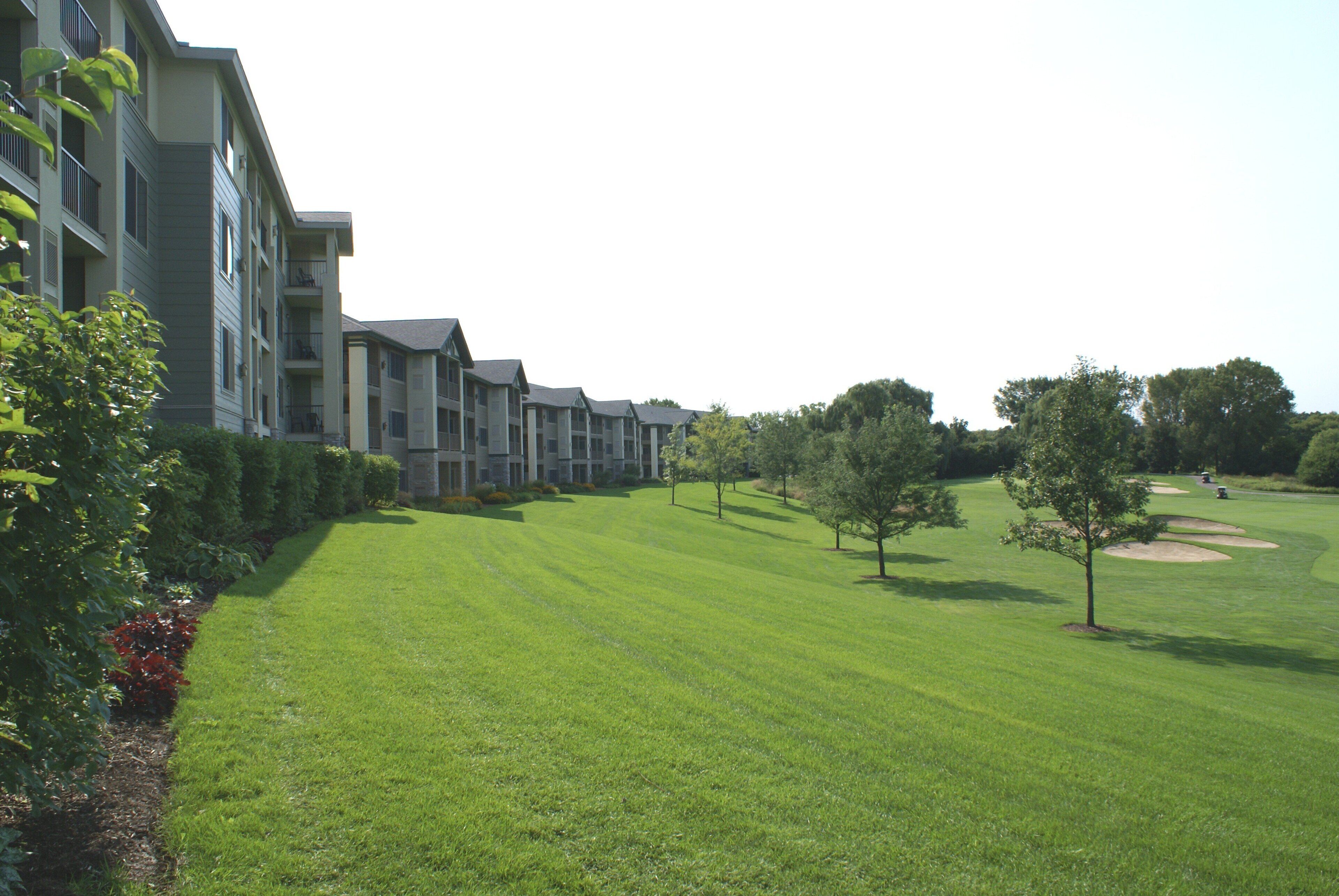 A row of multi-story residential buildings with a well-maintained lawn and trees.