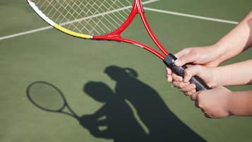A tennis racket and a shadow of a person playing tennis on a green court.