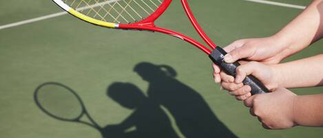 Una raqueta de tenis y la sombra de una persona jugando al tenis en una cancha verde.