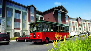 A red trolley with "The Grand Trolley" written on it, parked in front of a building with large windows and stone accents. - Holiday Inn Club Vacations at Lake Geneva Resort by IHG (Lake Geneva)