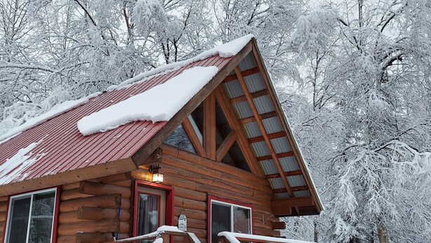 A wooden cabin with a red roof, a porch, and a staircase leading to the entrance. - Hatcher Pass Cabins (Palmer)