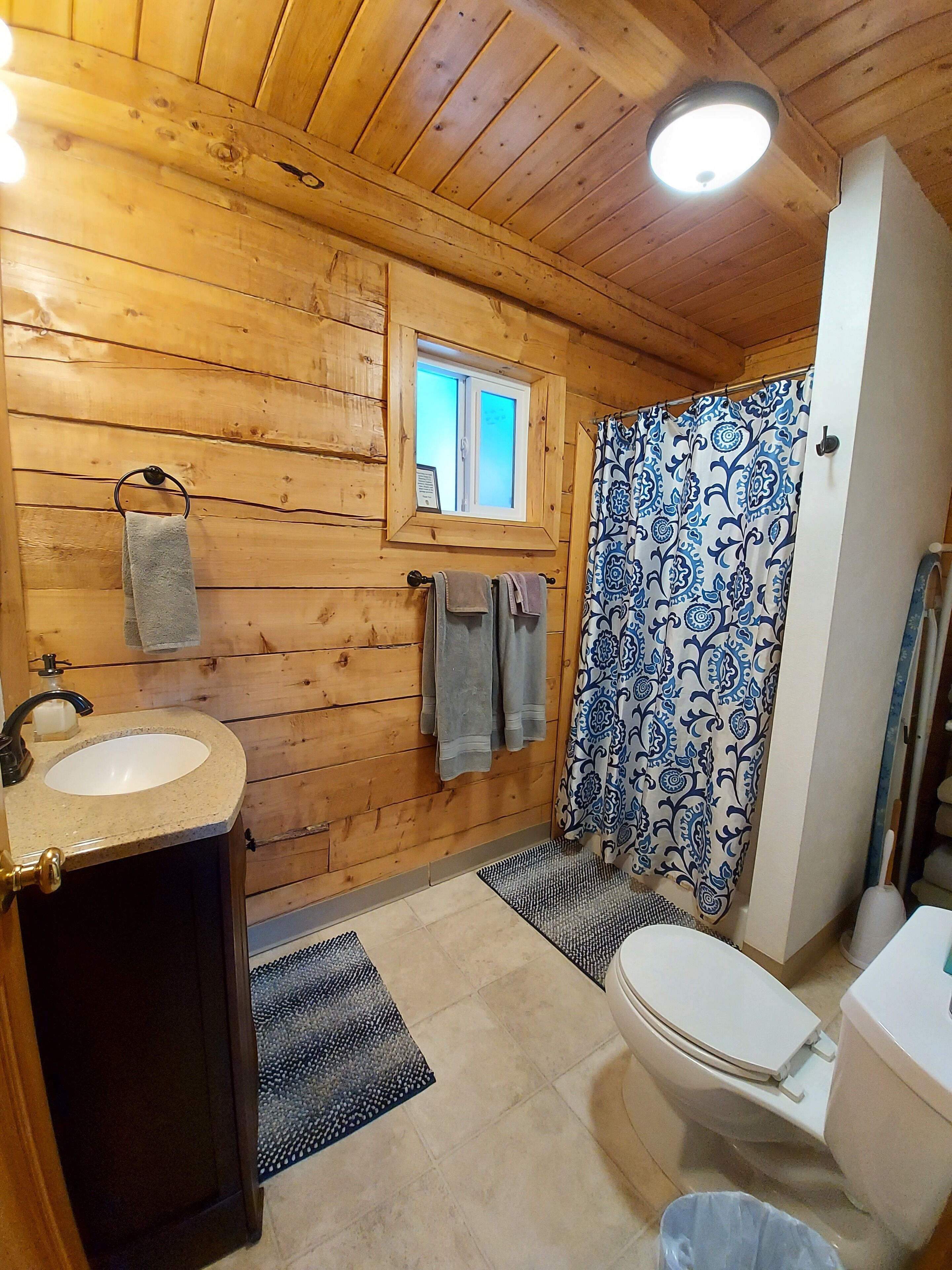 A wooden cabin bathroom with a sink, toilet, and shower curtain.