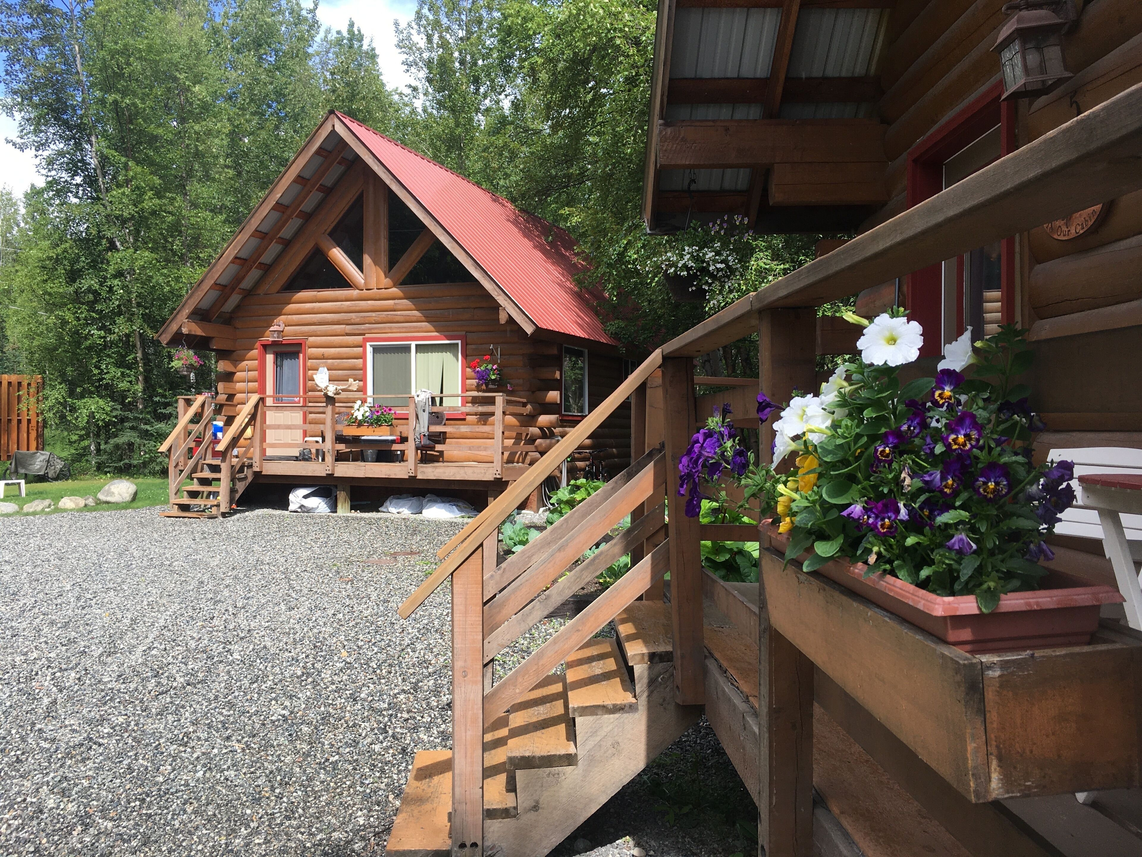A wooden cabin with a red roof, a wooden deck, and a staircase leading to the entrance.