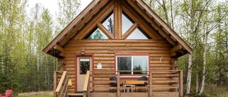 Een vakantiehuisje van hout met een houten terras, een voordeur en een raam.