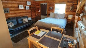 A cozy log cabin room with a bed, a sofa, a dining table, and a ceiling fan. - Hatcher Pass Cabins (Palmer)