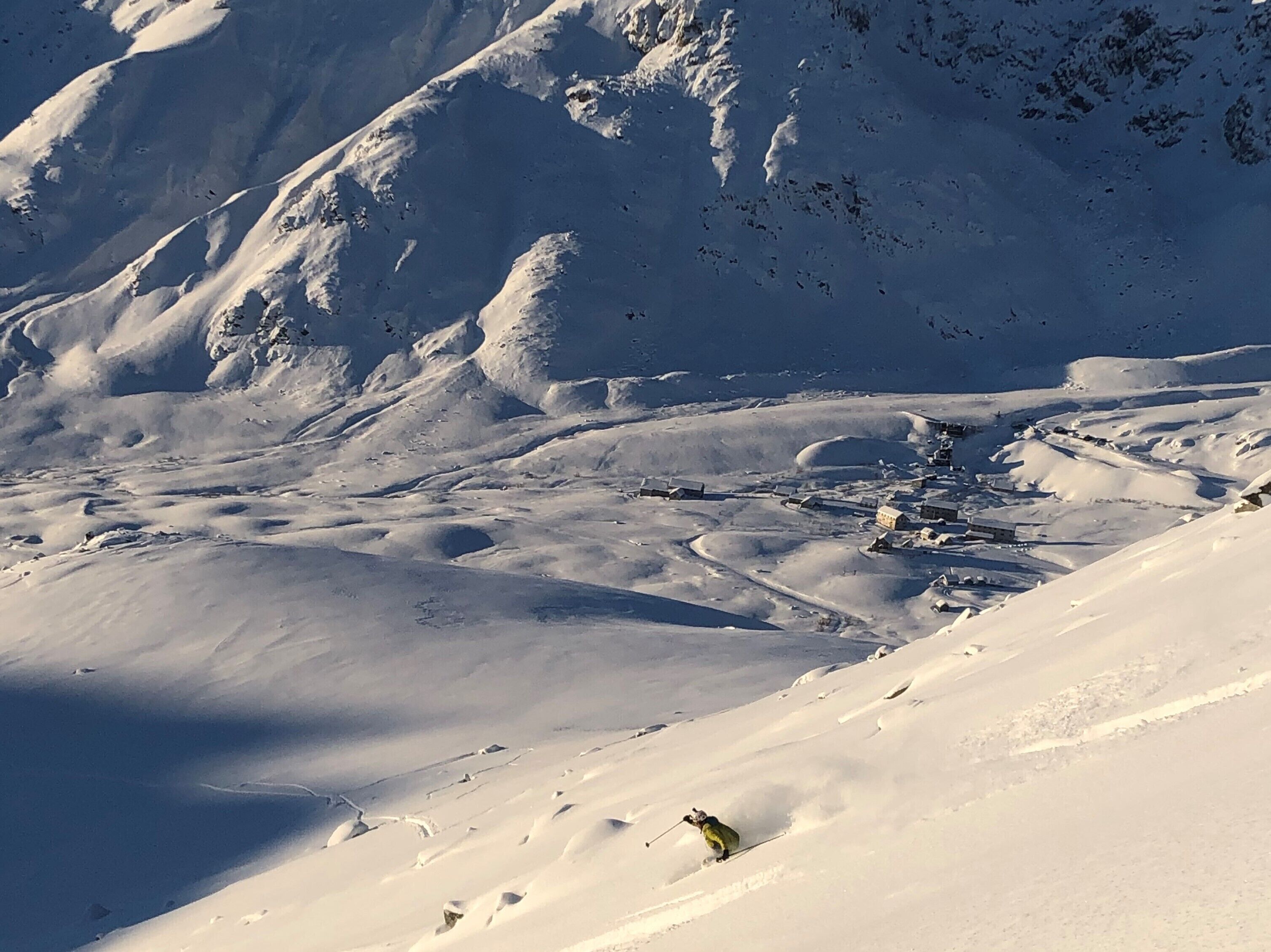 Un paisaje montañoso nevado con una pista de esquí y un pequeño asentamiento a la base.