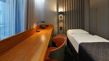 Une chambre d’hôtel avec un bureau en bois, un lit, une chaise, une table de chevet, une lampe et une fenêtre avec des rideaux.
