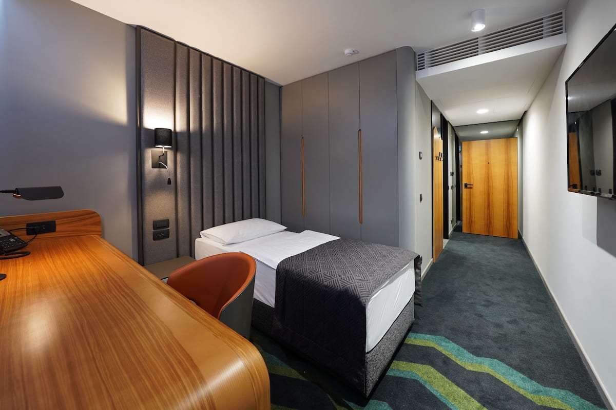 A hotel room with a bed, a desk, a chair, a wardrobe, and a mirror.