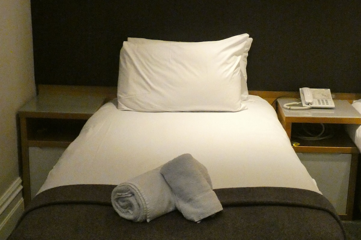 Habitación de hotel con cama, mesita de noche y teléfono, y una pared con diseño decorativo.
