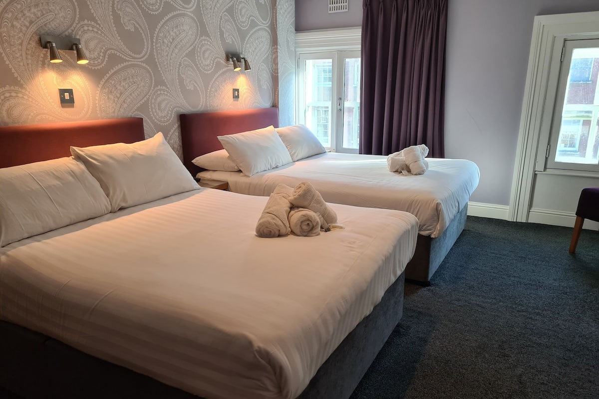 Habitación de hotel con dos camas, cada una con ropa blanca y almohadas, y un par de toallas sobre las camas.