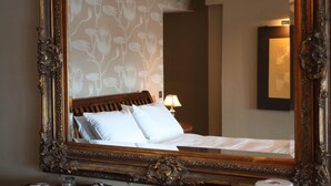 Une chambre d’hôtel dotée d’un grand miroir décoratif qui reflète un lit aux draps blancs et une table de chevet avec une lampe.