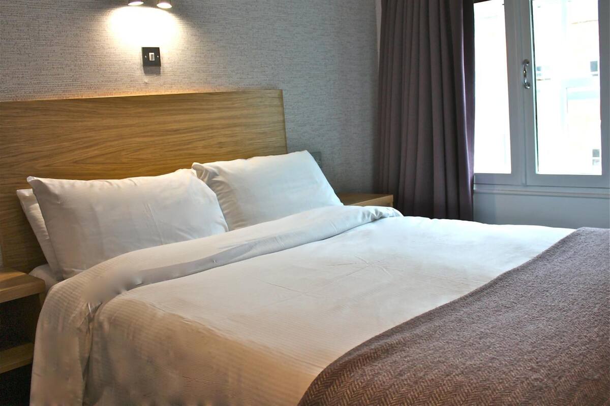 Una cama bien hecha con cabecera de madera, una mesita de noche y una lámpara de pared.