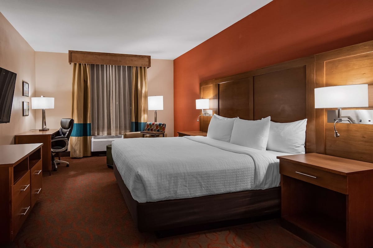 Quarto de hotel com cama, escrivaninha, cadeira, televisão e duas luminárias.