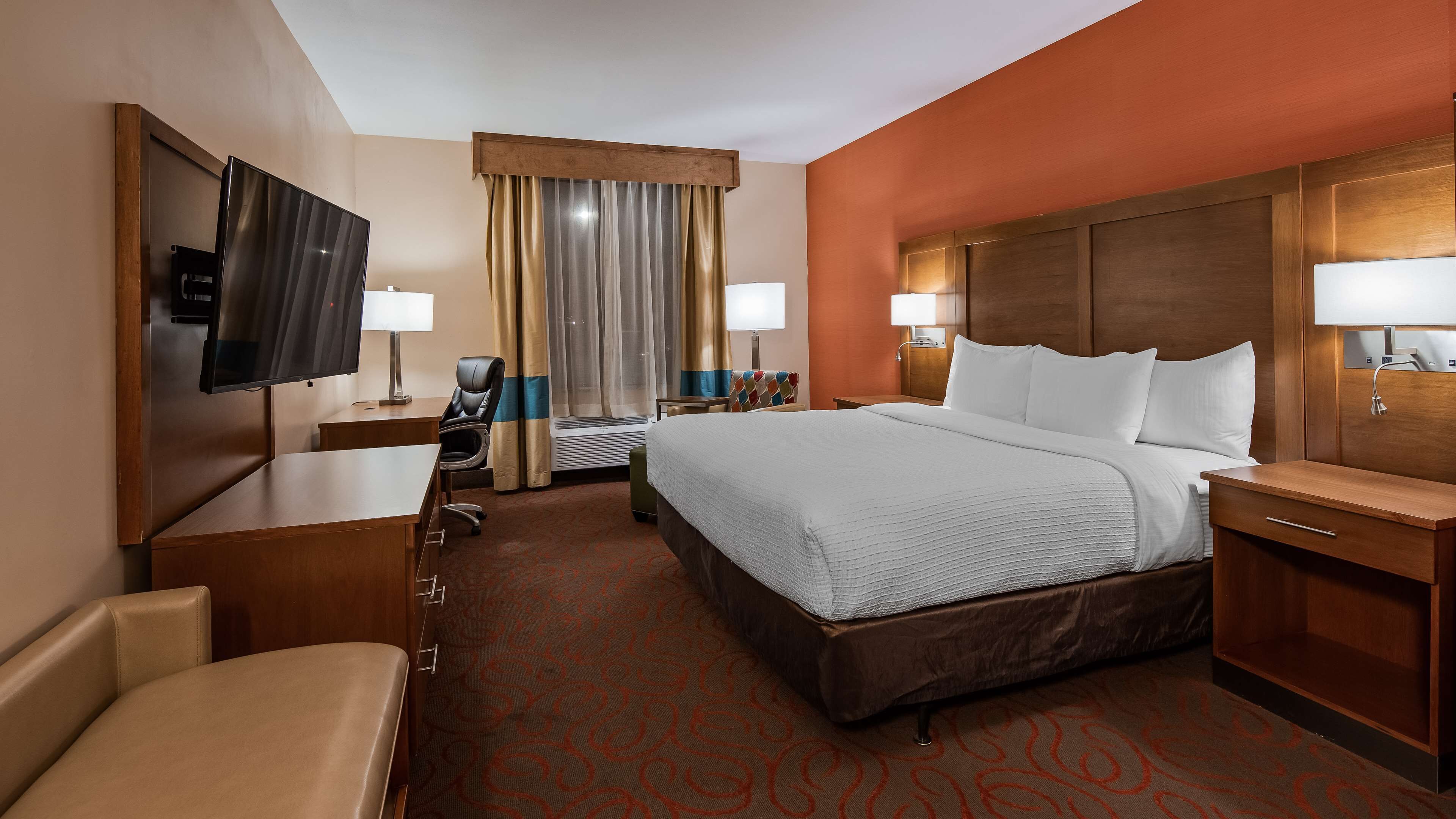 A hotel room with a large bed, a desk with a chair, a TV, and two bedside lamps.
