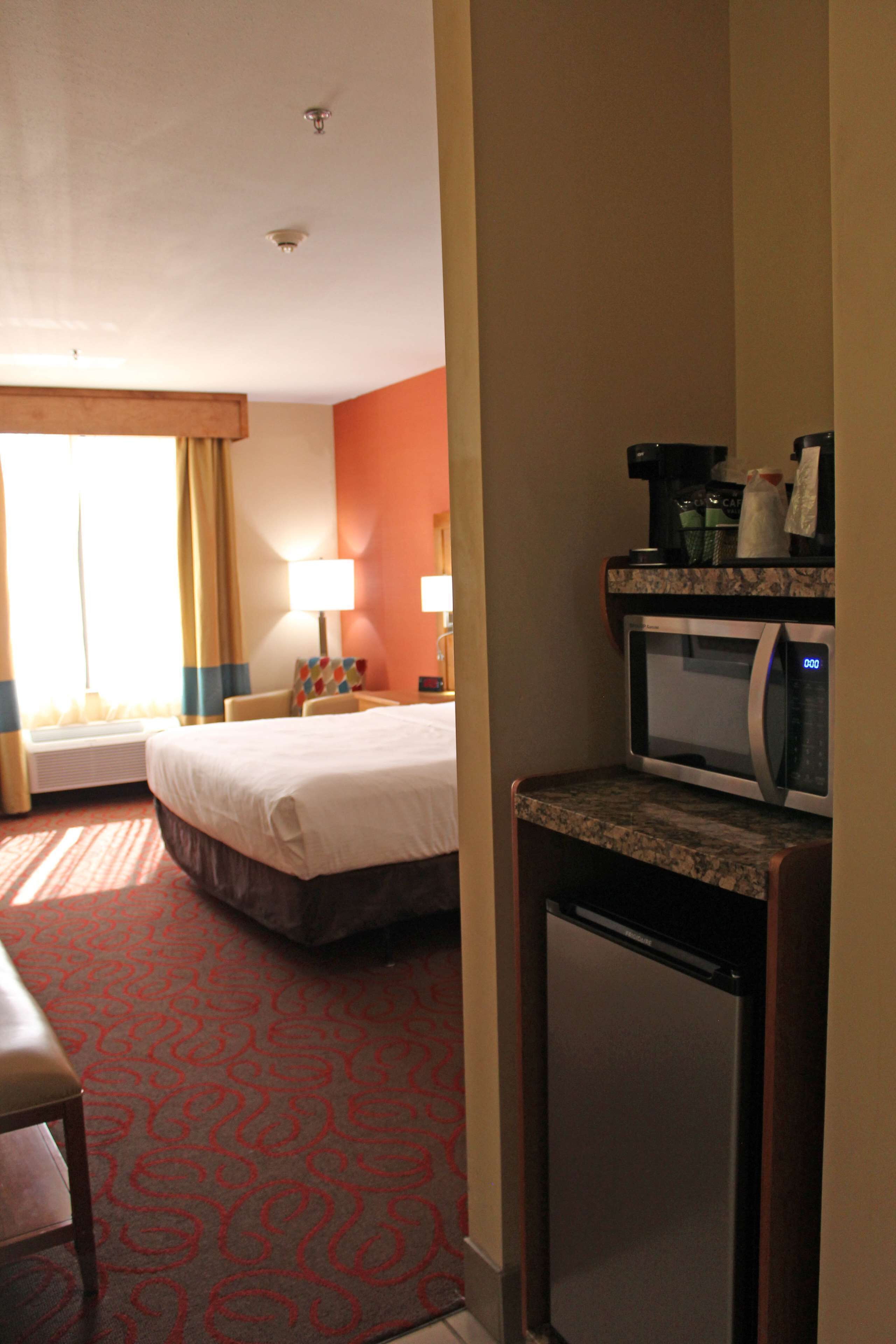 A hotel room with a bed, a desk, a microwave, and a small refrigerator.