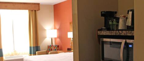 A hotel room with a bed, a desk, a microwave, and a small refrigerator.