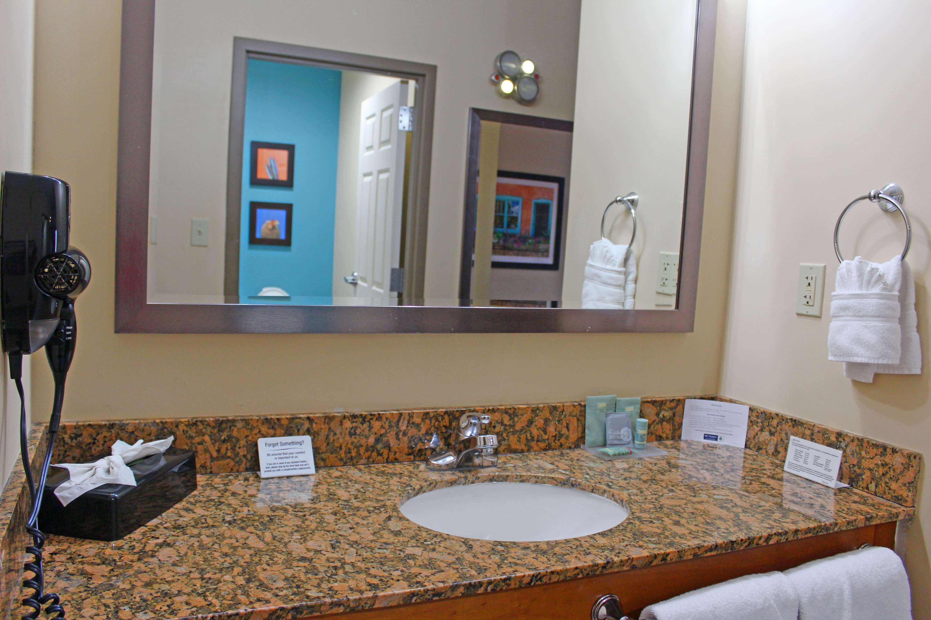 A bathroom with a granite countertop, a white sink, a large mirror, and a hair dryer on the left.