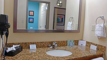 A bathroom with a granite countertop, a white sink, a large mirror, and a hair dryer on the left.