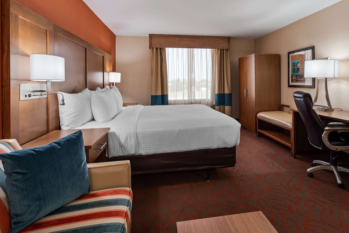 Quarto de hotel com cama, escrivaninha, cadeira, sofá e janela com cortinas.