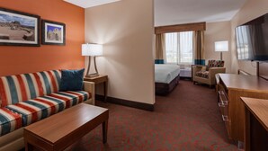 Hotelkamer met een gestreept bankje, een bed, een bureau, een televisie en twee ingelijste foto's aan de muur.