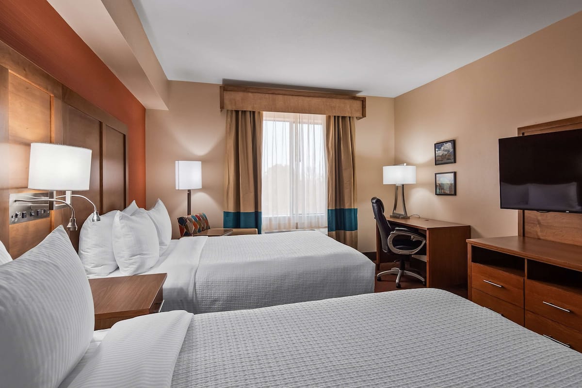Quarto de hotel com duas camas, uma escrivaninha, uma cadeira, uma televisão e uma janela com cortinas.