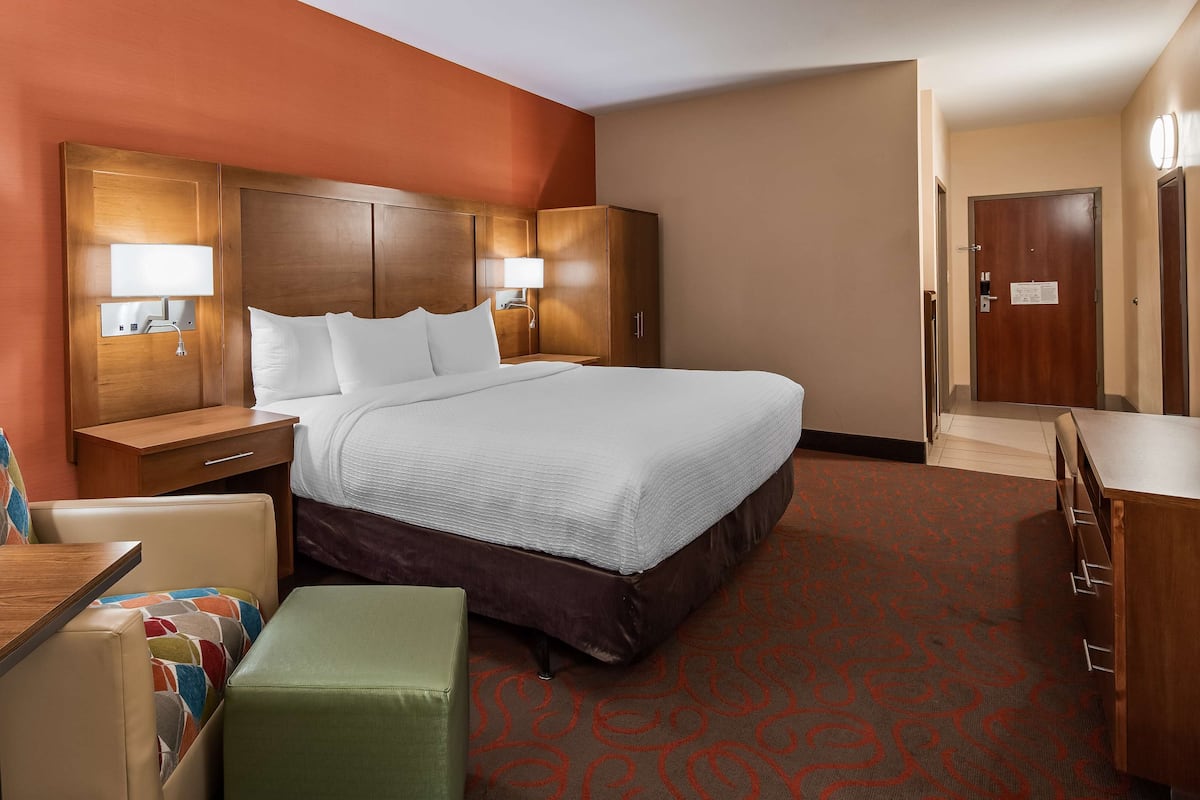 Quarto de hotel com cama, escrivaninha, cadeira e mesa pequena.