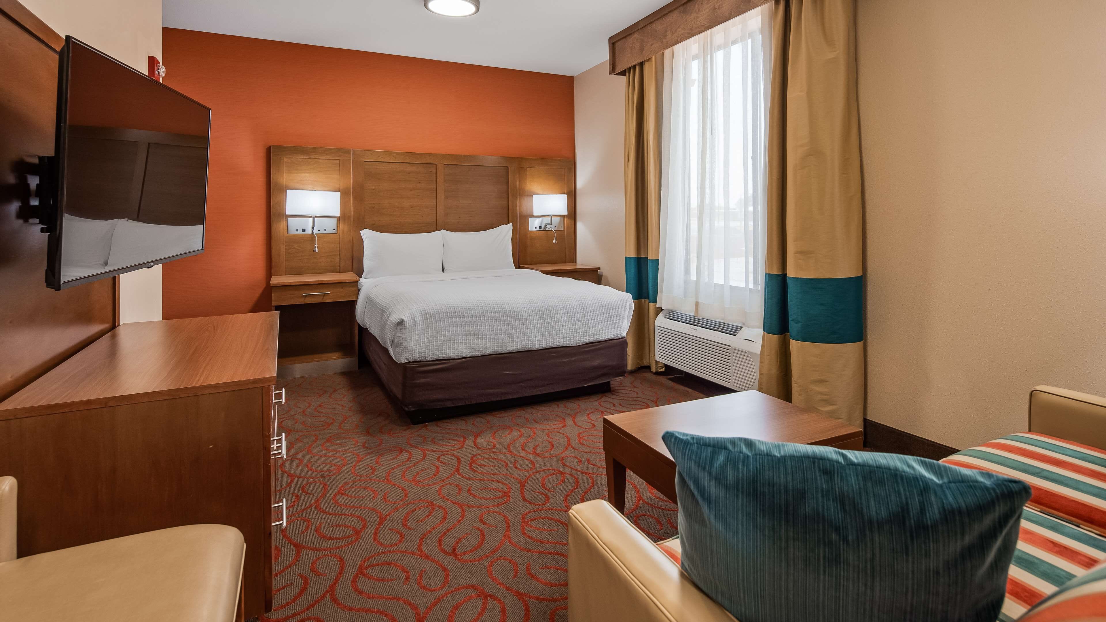 A hotel room with a bed, a desk, a chair, a TV, and a window with curtains.