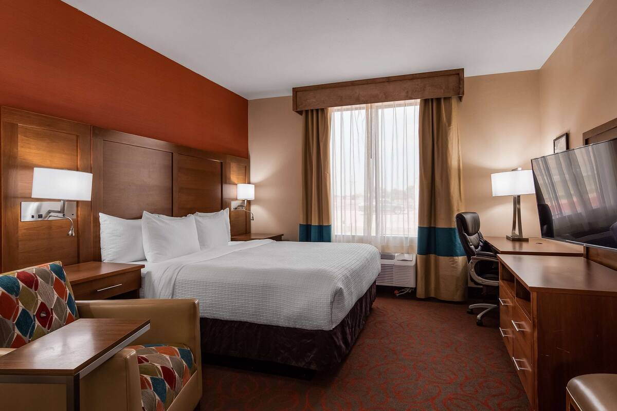 Quarto de hotel com cama, secretária, televisão e cadeira.