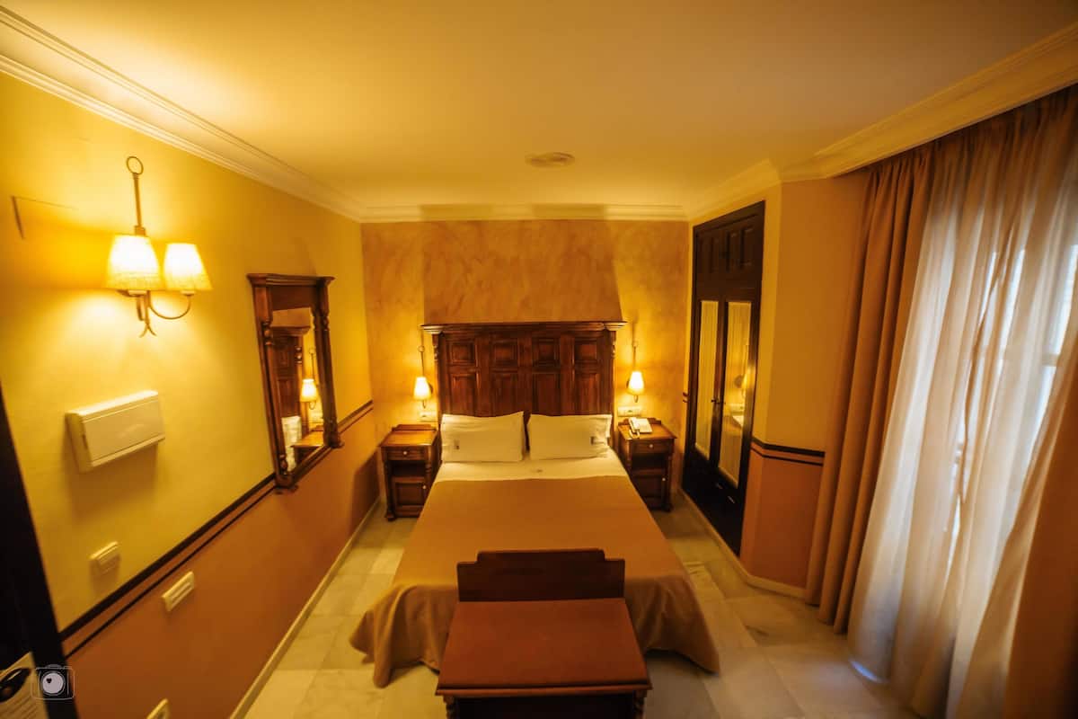 Ein Hotelzimmer mit einem großen Bett, Nachttischen, einem Spiegel und einem Fenster mit Vorhängen.