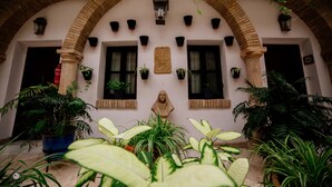 A courtyard with a brick archway, potted plants, and a bust sculpture. - Hotel Posada de Vallina by MiRa (Córdoba)