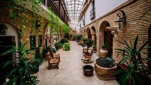 An indoor courtyard with stone walls, arches, and hanging plants. There are wooden chairs and a large pot on the ground. - Hotel Posada de Vallina by MiRa (Córdoba)
