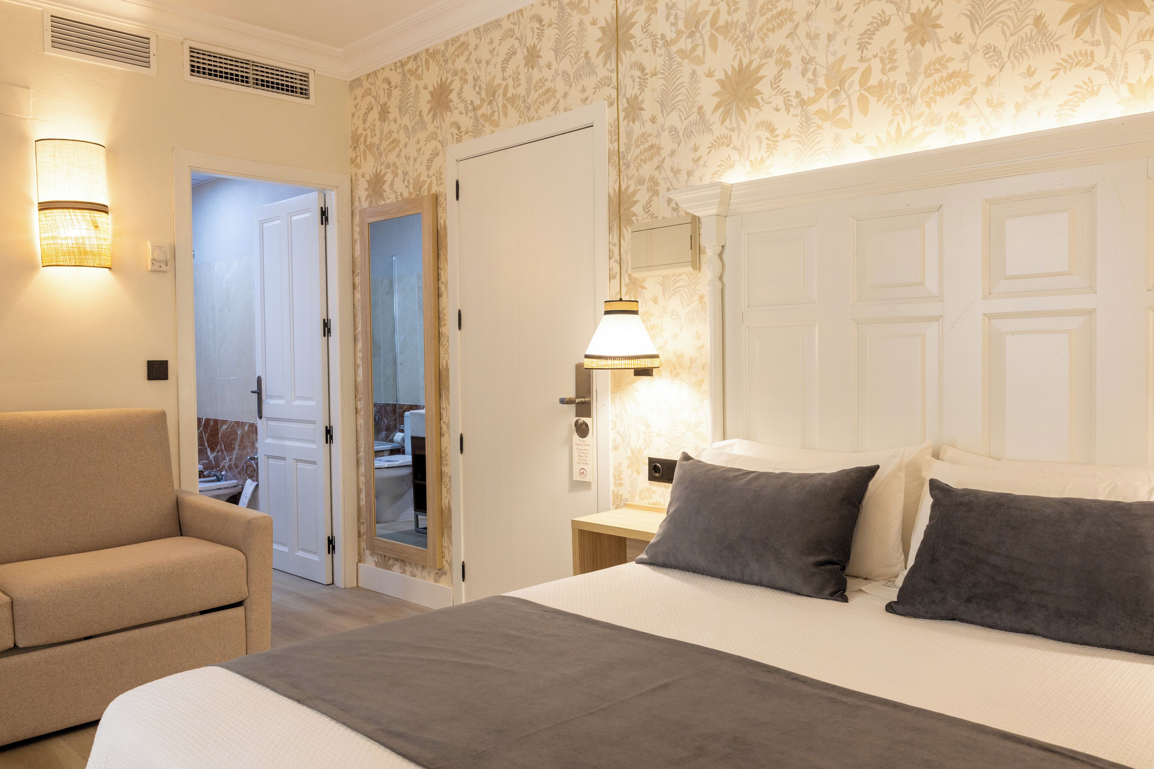 Une chambre d’hôtel avec un lit, une chaise, une table de chevet et une salle de bain visible à travers une porte ouverte.