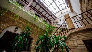 A spacious atrium with a high ceiling, stone walls, and a staircase with a wrought iron railing. - Hotel Posada de Vallina by MiRa (Córdoba)