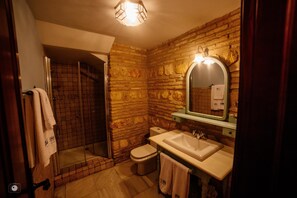 A bathroom with a stone wall, a shower, a toilet, and a sink.
