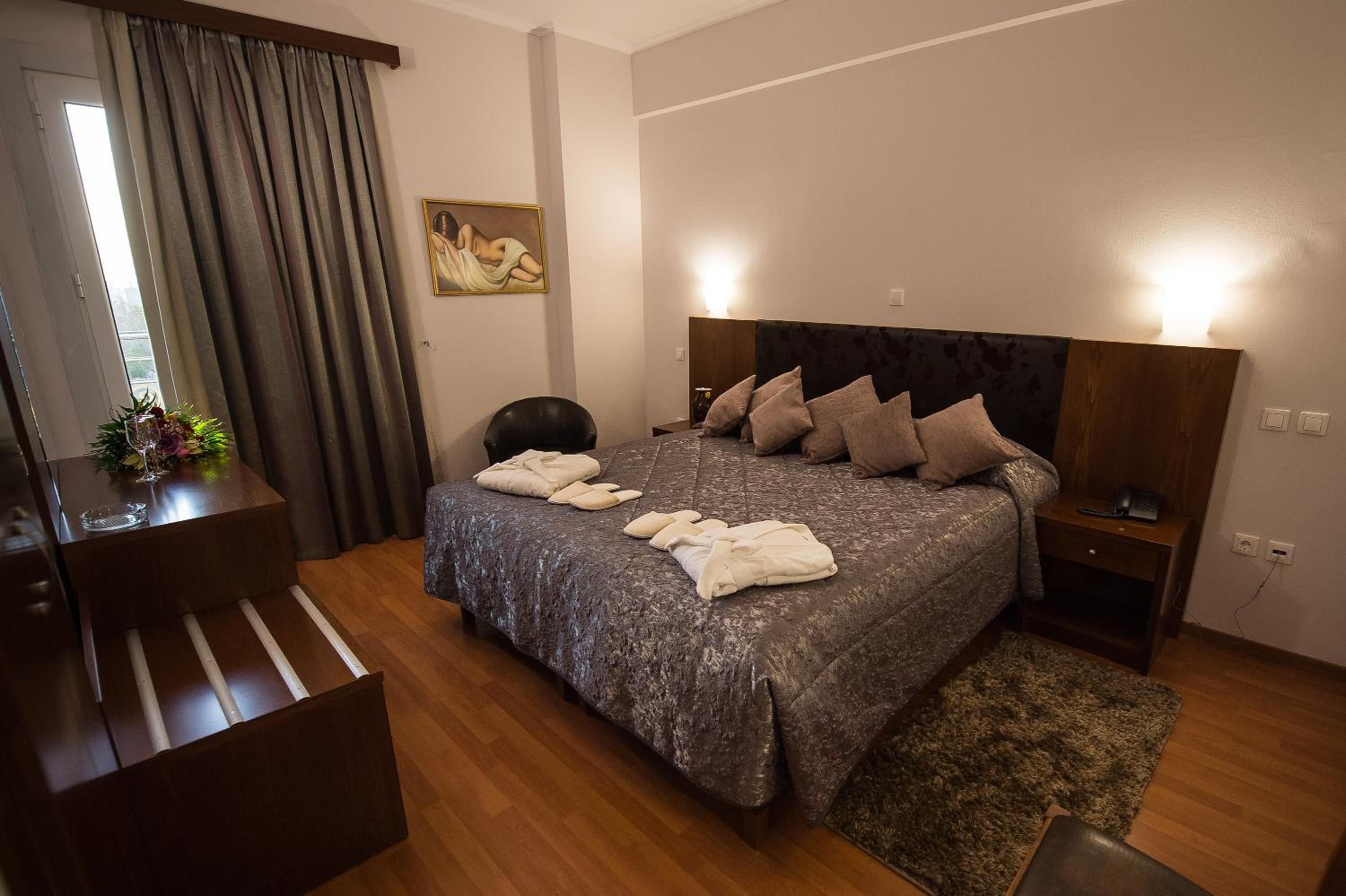 A hotel room with a bed, bedside tables, a desk, and a painting on the wall.