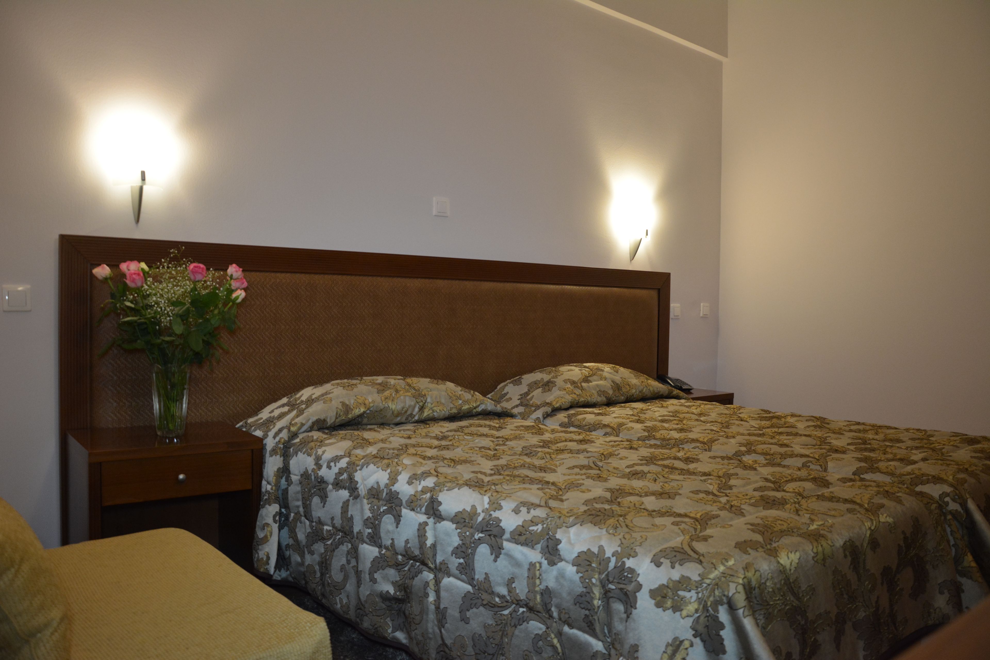 Ein Schlafzimmer mit einem Bett, einem Nachttisch mit Blumenvase und zwei Wandleuchten.